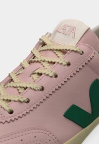 Αθλητικό παπούτσι από ανοιχτό ροζ δέρμα με μπεζ κορδόνια, πράσινο λογότυπο και αντίθετη ραφή. Στρογγυλή μύτη και υφή στη σόλα.