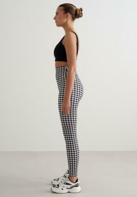 Czarny krótki top zestawiony z legginsami z wysokim stanem w czarno-biały wzór pepitki. Noszony z białymi i czarnymi trampkami.