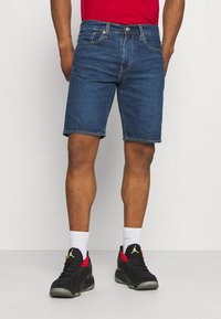 Tmavě modré džíny s rovný střih, které mají pět kapes, poutka na pásek a mírné třepení na lemu, kombinované s černými teniskami.