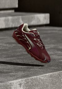 Bordo un unbeige sporta apava ar liesmu dizainu, saites sasietas, plunčā virs pelēkām betona pakāpēm, radot ēnu.