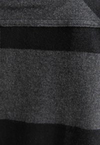 Grå och svart randig tyg med en mjuk struktur. Synliga sömmar längs kanterna. Designen har växlande horisontella band.