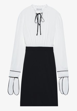 White blouse with a gathered neckline and drawstring; black fitted skirt with contrasting white piping on the sleeves. Smooth fabric texture.