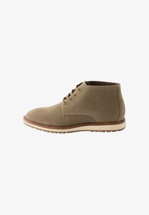 Bottines en suède vert olive avec six œillets, détails contrastés en surpiqûre, et une semelle en caoutchouc léger avec un contour marron.