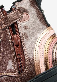 Brązowe, błyszczące dziecięce buty z brązowym zamkiem błyskawicznym, rzepem oraz różowymi i złotymi haftowanymi paskami po bokach.