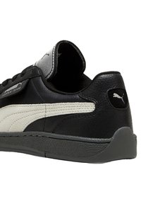 Sneaker in pelle nera con dettagli bianchi, superficie strutturata, collo imbottito e suola in gomma grigia. Logo Puma sul tallone.