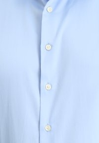Lichtblauw overhemd van gladde stof, voorzien van zes enkele knopen met een helder ontwerp en witte ronde accenten.