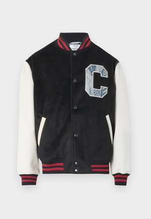 Schwarze Collegejacke mit weißen Ärmeln, rot-schwarz gestreiftem Kragen und Bündchen, Druckknöpfen und einem großen, strukturierten blauen "C" auf der Brust.
