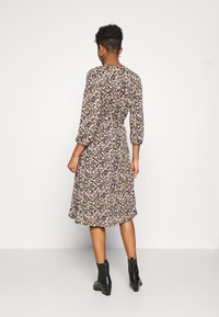 Sukienka w kwiaty z rękawami o długości trzy czwarte, na czarnym tle, z wielokolorowymi małymi kwiatami, z wiązaniem w talii, do kolan, zestawiona z botkami za kostkę.