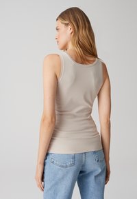 Haut beige sans manches avec une coupe ajustée et un col rond, associé à un jean en denim bleu clair avec poches arrière. Texture lisse.