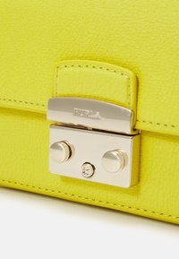 Borsa a tracolla in pelle gialla con finitura texturizzata, dotata di chiusura e hardware in metallo argentato, logo impresso e dettagli cuciti.