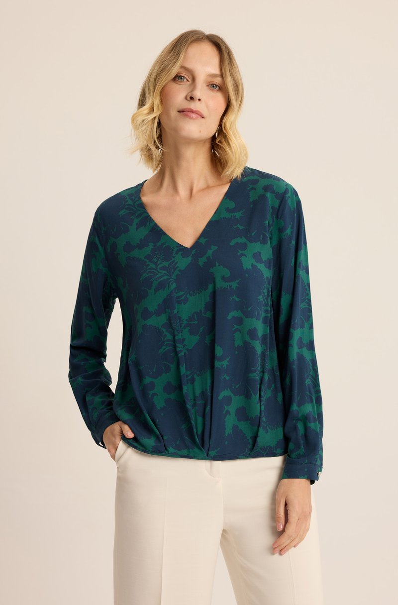 Czarna bluzka z długim rękawem w ciemnozielonym kolorze z kwiatowym wzorem. Posiada głęboki dekolt w serek oraz marszczenie w talii, zestawiona z jasnymi spodniami.