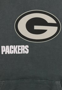 Mörkgrå huvtröja med en stor svart och vit cirkulär "G"-logotyp och texten "PACKERS" i fet vita bokstäver. Mjuk tygkänsla.