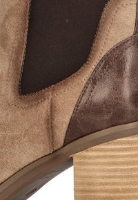 Botín de ante marrón con un panel elástico negro y un tacón texturizado marrón. Presenta un acento de cuero liso y una silueta estructurada.