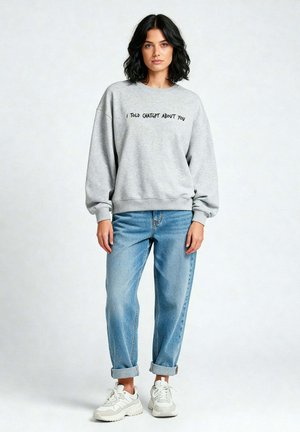 Grijze sweatshirt met de tekst "IK HEB CHATGPT OVER JOU GEVENDE", relaxed fit, gecombineerd met lichtblauwe jeans en witte sneakers. Casual outfit.