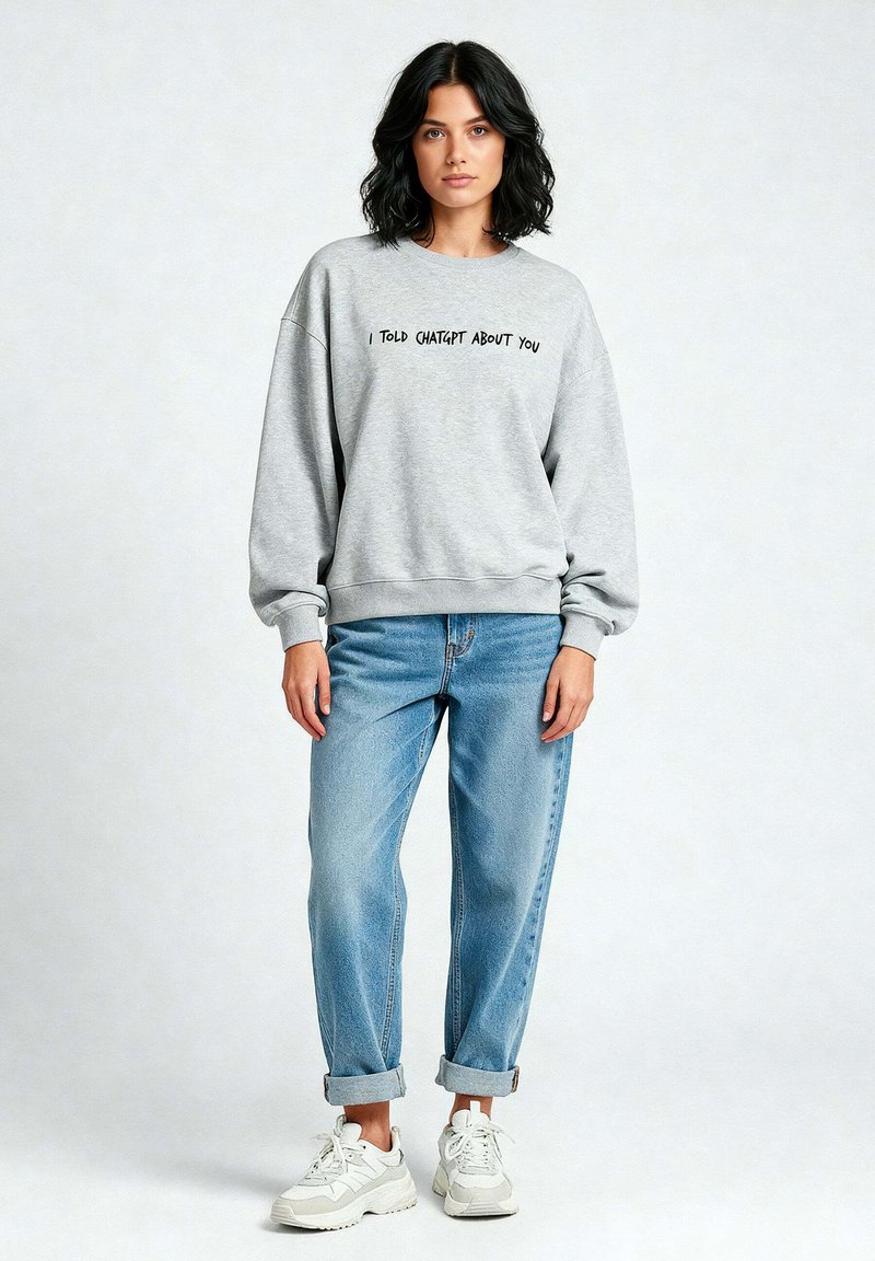 Felpa grigia con la scritta "HO PARLATO DI TE A CHATGPT", vestibilità rilassata, abbinata a jeans azzurri chiari e sneakers bianche. Outfit casual.