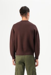 Suéter de punto marrón con escote redondo, puños acanalados y dobladillo, combinado con pantalones cargo verde oliva que cuentan con bolsillos laterales.
