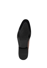 Suela de zapato de cuero marrón con un inserto de goma negra texturizada, que presenta una forma curvada y costuras detalladas a lo largo del borde.