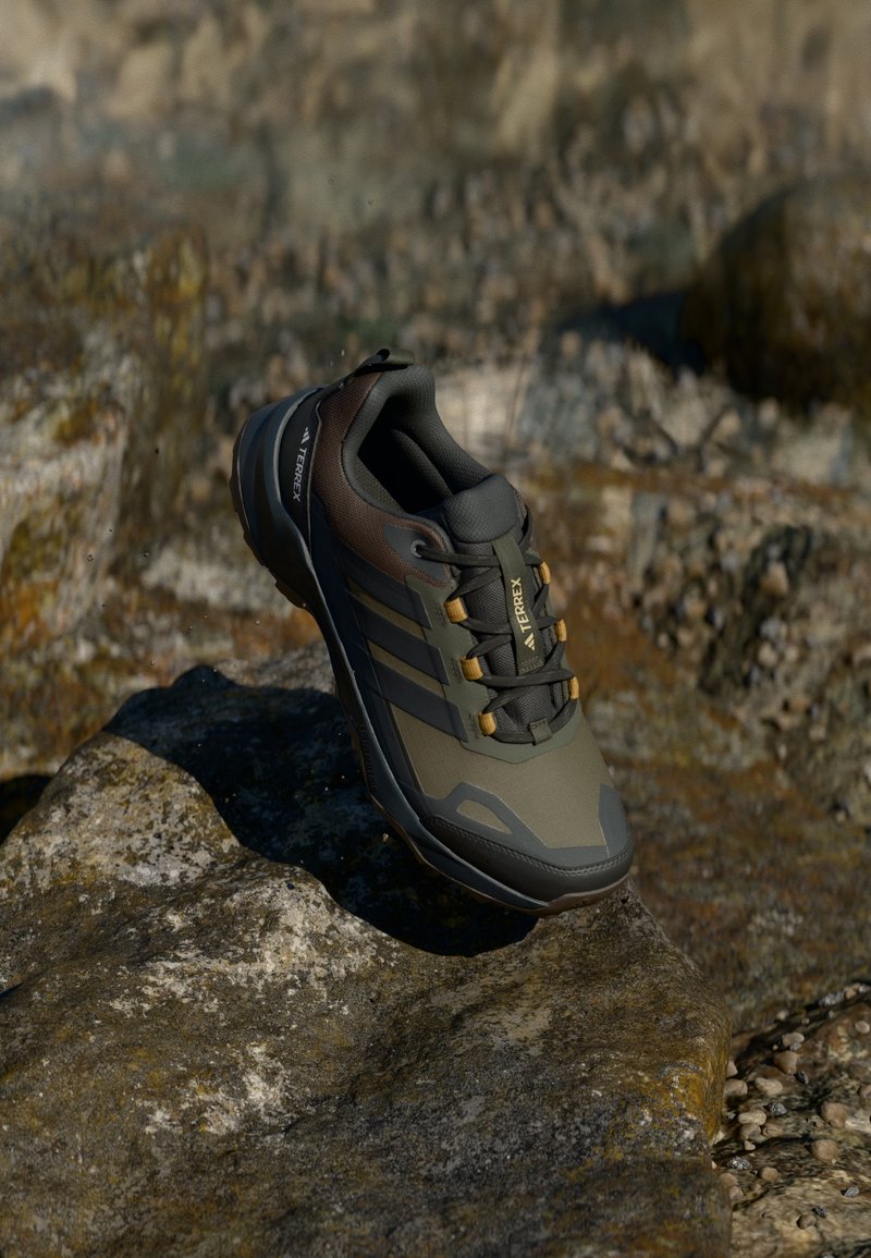 Terrex Schuhe in Grün und Braun mit einer strukturierten Oberseite, verstärkter Zehenkappe und schwarzer Sohle. Mit goldenen Akzenten und einem sicheren Schnürsystem ausgestattet.