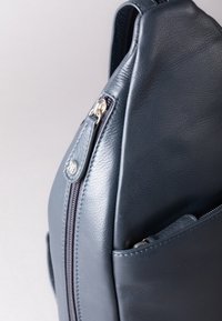 Dark blue leather bag with a textured surface, featuring a silver zipper and a small front pocket. The design is sleek and angular.