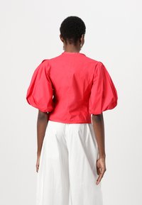 Cropped shirt rossa con maniche a sbuffo, realizzata in tessuto leggero. Linee pulite e design semplice, abbinata a pantaloni bianchi larghi.