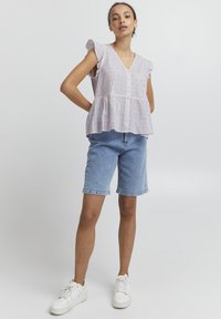 Haut en lin violet clair avec des manches courtes à volants, fermeture à boutons et ourlet peplum, associé à un short en denim bleu clair et des baskets blanches.