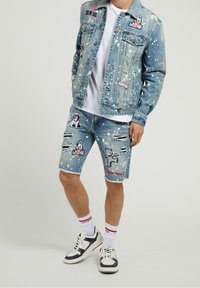 Jeansjacka och shorts set i ljusblå tvätt, målade splatter, broderade lappar, slitna detaljer och svarta detaljer. Vit T-shirt och sneakers.