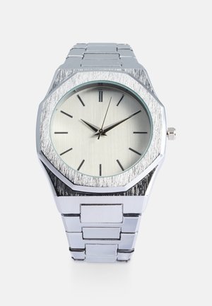 Hõbedane roostevabast terasest kell, millel on kaheksanurkne korpus, harjatud tekstuur, minimaalselt hele hõbedane sihtplaat ja mustad tundemärgid. Metallist link-rihm.