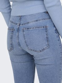 High-waisted, light blue denim jeans with a slim fit, featuring two back pockets and contrasting stitching. Smooth texture with slight stretch.