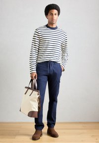 Navy cargo bukser og en cremet stribet langærmet skjorte, med en brun læder-accentueret tote taske. Sættet har et enkelt, funktionelt design.
