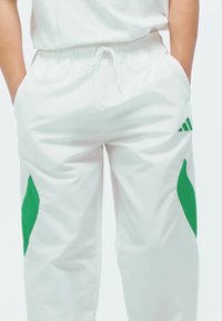Bijele atletske hlače s zelenim akcentima sa strane, elastičnim pojasom i džepovima, izrađene od glatkoga, laganog materijala.