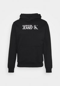 Felpa nera in cotone con tasca a marsupio. Presenta un testo stampato in bianco: "CALVIN KLEIN JEANS" e un logo "CK" sul davanti.