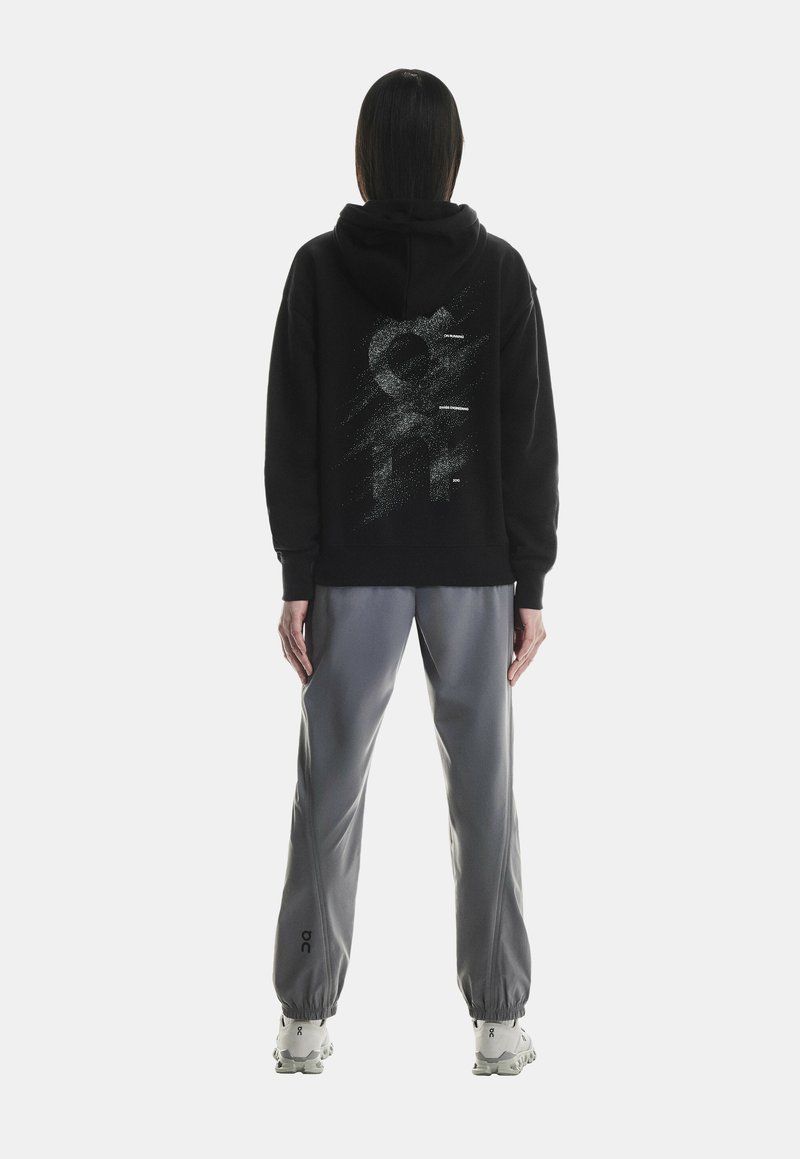 Must musta, millel on seljal tekstureeritud, abstraktne graafika, koos hallide kitsaste dressipükstega. Kingadel on külje peal logo.