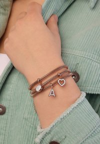 Roze gouden armbanden met een ronde bedel, een letter "A" en een hartbedel, met gestructureerde meshbanden en fonkelende accenten.