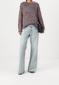 Pull en tricot texturé multicolore à manches longues, associé à un jean en denim bleu clair à jambes larges et un petit sac à main noir.