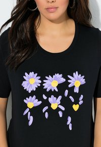 Czarna koszulka z nadrukiem kwiatowym, przedstawiającym pięć fioletowych stokrotek o żółtych środkach, ozdobionych rozproszonymi płatkami i sercami. Krótkie rękawy.