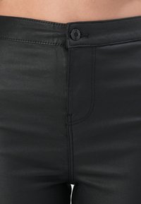 Czarne spodnie z ekologicznej skóry o gładkiej fakturze, z zapięciem na guziki z przodu, szlufkami na pasek i subtelnym detalem przeszycia.