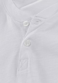 Weißes Baumwollhemd mit V-Ausschnitt, das drei weiße Knöpfe und eine diagonale Nahtdetails in der Nähe der Knopfleiste aufweist. Weicher, strukturierten Stoff.