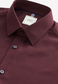 Camicia da uomo bordeaux con trama, colletto strutturato, due bottoni scuri e etichetta con strisce.
