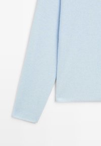 Manica e lato di un maglione a maglia azzurro chiaro mostrati su sfondo bianco, evidenziando la texture del tessuto e i bordi puliti.