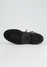 Suela de bota de goma negra con profundas ranuras para tracción, con un detalle de logotipo. El material tiene una textura con un diseño angular.