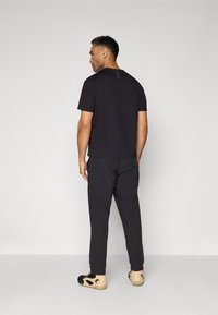 Black t-shirt with short sleeves, paired with black pants and beige shoes. Simple design, no visible patterns or logos.