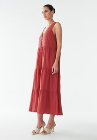 Ruudukarva värvi maxi-kleit sügava V-kaelusega, ees nupud ja kihiline disain. Kangas näib kerge ja sile. Sobitatud punutud kontsakingadega.