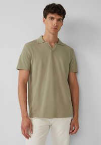 Olijfgroen poloshirt met korte mouwen en een V-halsontwerp, gemaakt van zachte stof, in combinatie met lichte broeken.