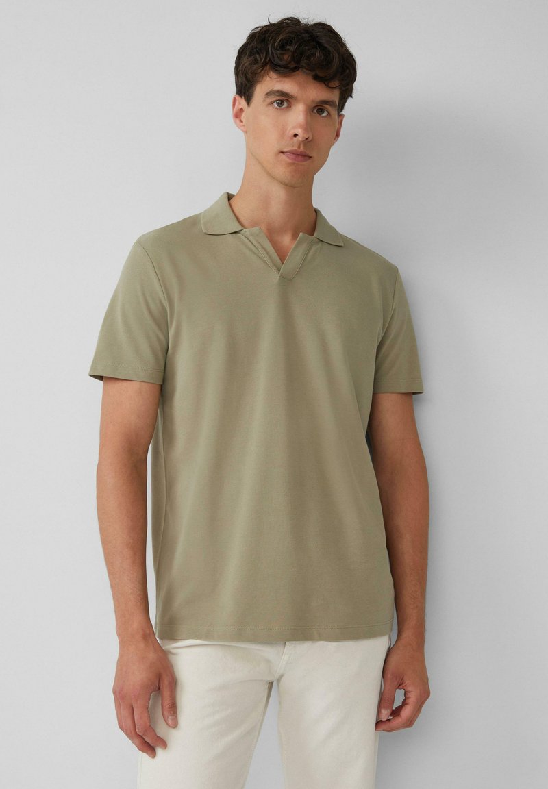 Olijfgroen poloshirt met korte mouwen en een V-halsontwerp, gemaakt van zachte stof, in combinatie met lichte broeken.