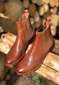 Bottines Chelsea en cuir marron avec des panneaux latéraux élastiques, des détails en brogue sur le bout et une texture contrastante. Talon empilé et boucle de tirage inclus.