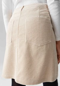 Beige corduroy rok met verticale ribbels, twee achterzakken, een rechte snit en gestikte zoom. De stof heeft een zachte, gestructureerde uitstraling.