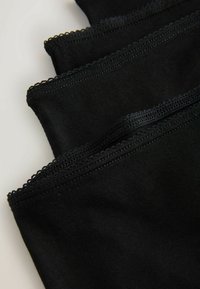 Štyri čierne textilné rúška s prešitými okrajmi a vlnitým lemom, vrstvené diagonálne na svetlom pozadí.