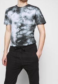 T-shirt gris tie-dye en coton doux, avec des manches courtes et un col rond, associé à un pantalon noir à coupe ample avec cordon de serrage.