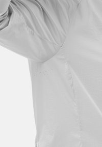 Lichtgrijs, lichtgewicht stoffen shirt met een gestructureerde afwerking, voorzien van een subtiel gestippeld patroon nabij de naad en een ronde halslijn.