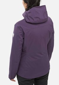 Person wearing a purple hooded jacket with a logo on the left arm, viewed from the back against a plain background.
